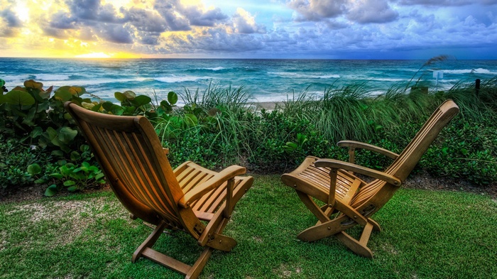 Two wooden chairs on a lawn overlooking the ocean
