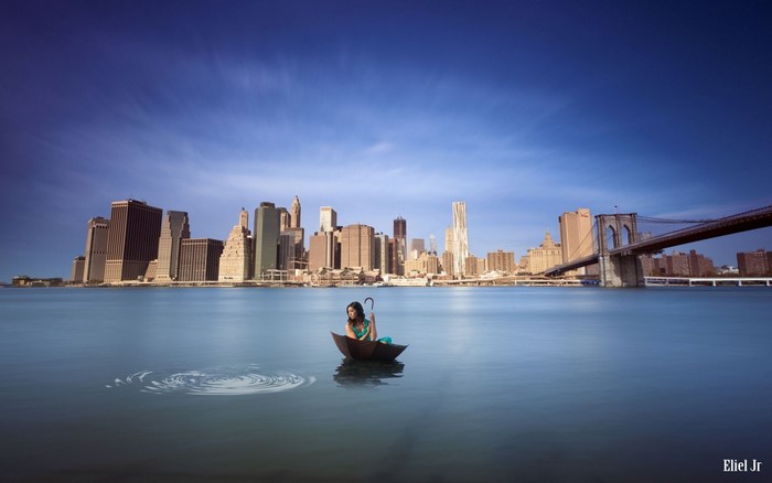 Woman in umbrella boat on water with New York City skyline