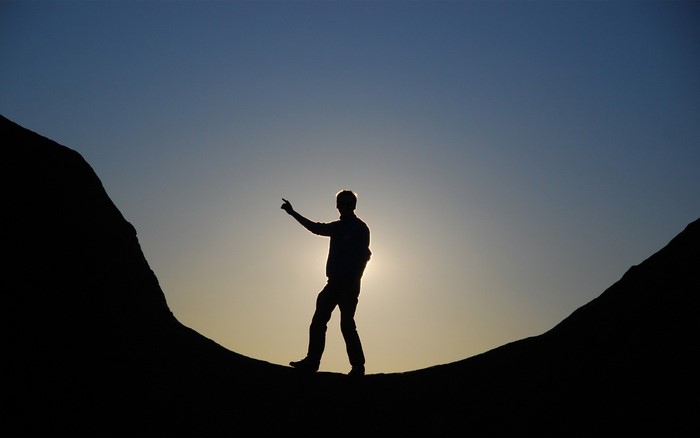 Silhouette of a man pointing at the sunset between mountains