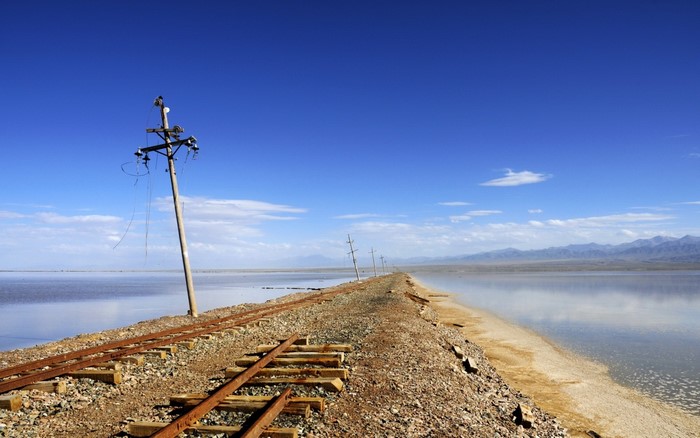 Abandoned railway tracks by a salt lake under a blue sky