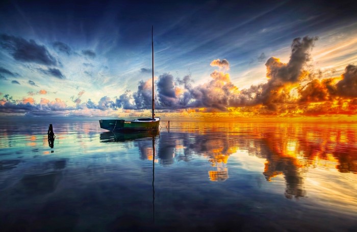 Sailboat on calm water at sunset with dramatic clouds