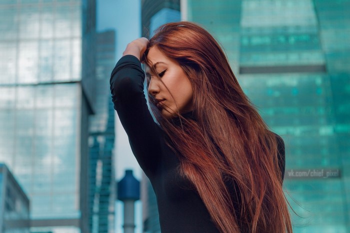 Woman with long red hair in front of modern buildings