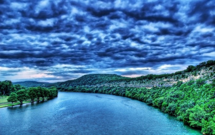 River flowing through a forested landscape under a cloudy sky