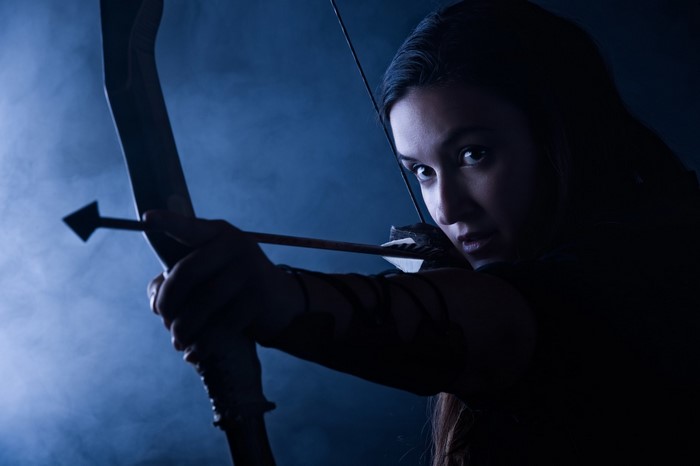 Woman aiming a bow and arrow in blue light