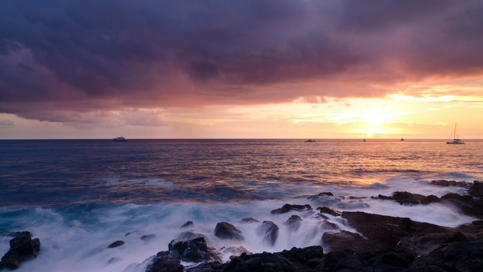 Sunset over the ocean with waves crashing on rocks