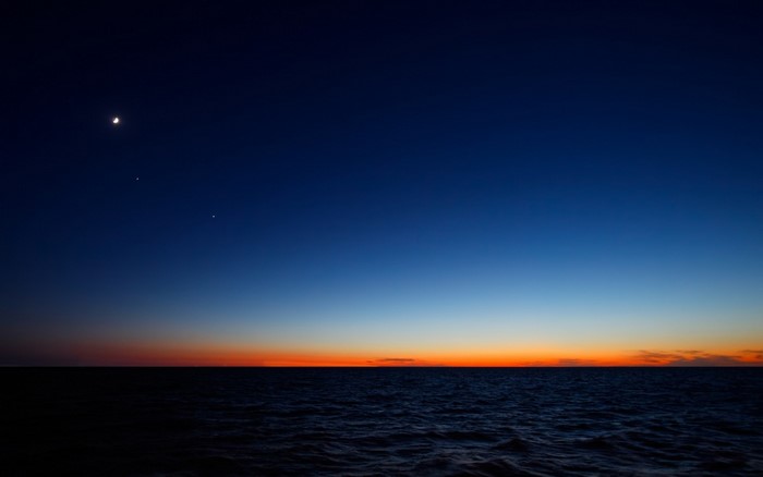 Crescent moon and planets over the ocean at dusk