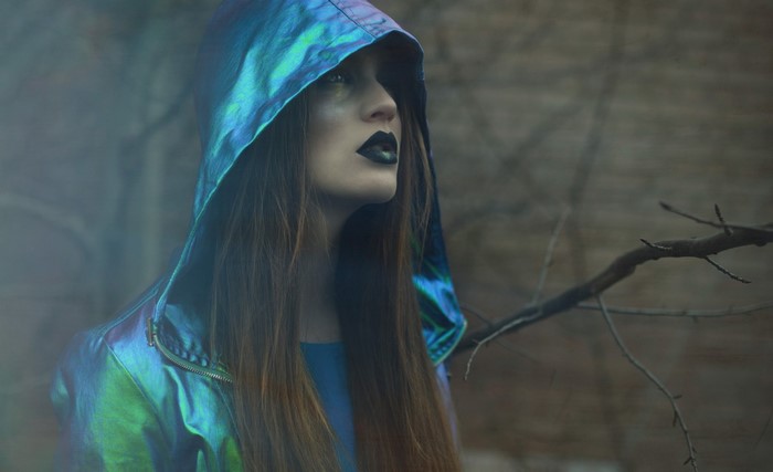 Woman in iridescent hooded jacket with dark makeup
