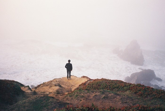 Person standing on a cliff overlooking a foggy sea