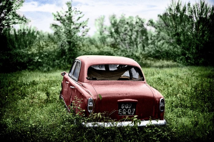 Abandoned red vintage car in a grassy field