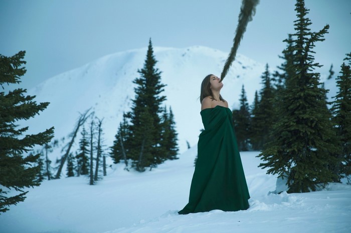 Woman in green dress exhaling smoke in snowy mountains