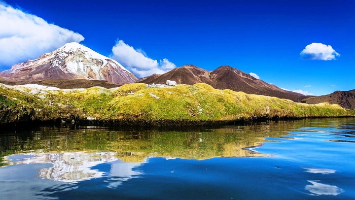 Snowy mountain reflected in a lake with green hills
