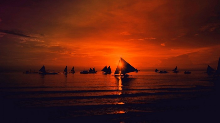 Sailboats silhouetted against a vibrant sunset over the ocean
