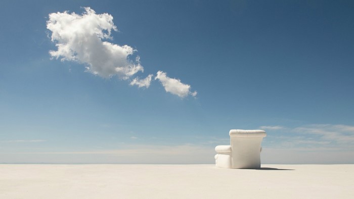 White armchair on a vast white plain under a blue sky with clouds