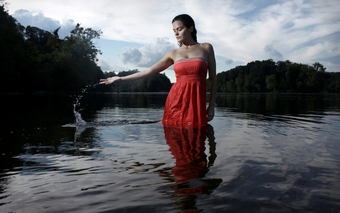 Woman in red dress splashing water in a lake