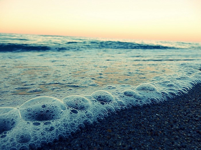 Ocean waves with bubbles on the shore at sunset