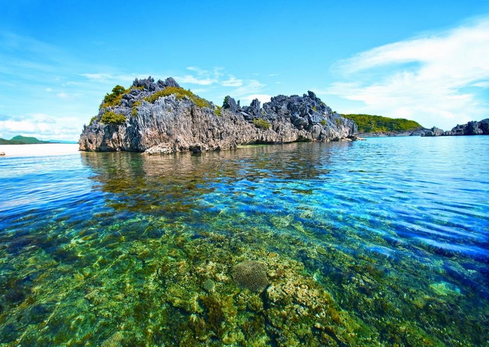 Rocky island in clear turquoise water with coral reef