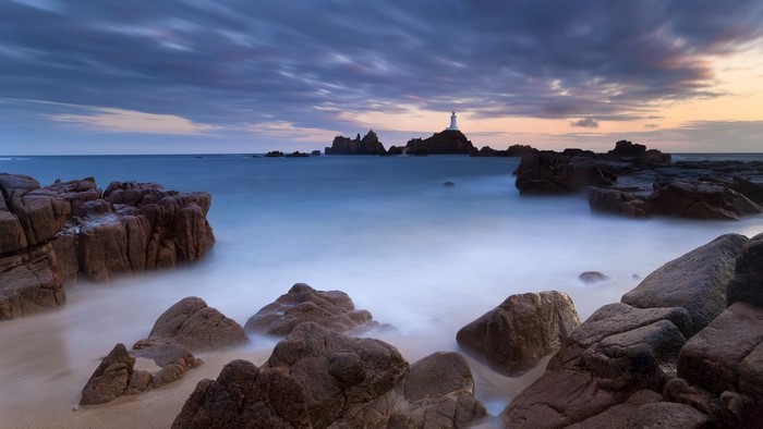 Lighthouse on rocky islands at sunset with long exposure sea