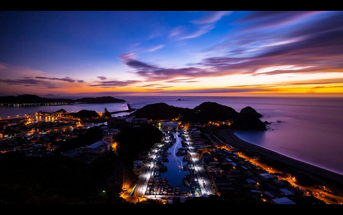 Coastal town at dusk with harbor lights and colorful sky
