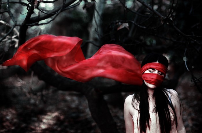 Woman blindfolded with red fabric in dark forest