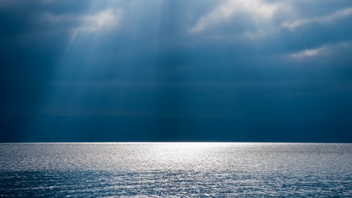 Sunlight beams through clouds onto the ocean horizon