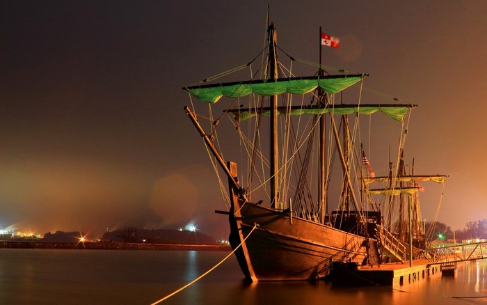 Tall ship with green sails docked at night