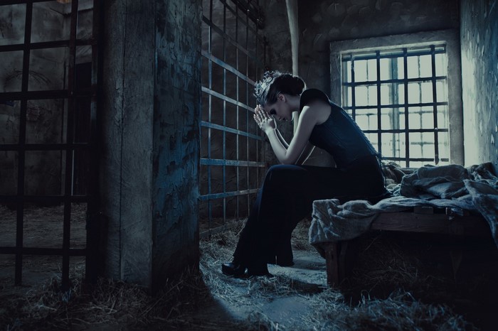 Woman praying in a dark prison cell