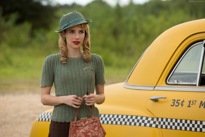 Emma Roberts in a green outfit and hat by a yellow taxi