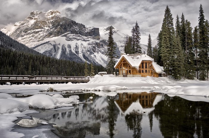 Wooden cabin by a frozen lake with snow-covered mountains