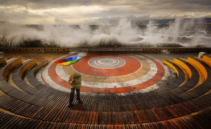 Person with umbrella in front of stormy sea and amphitheater