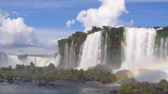 A wide waterfall cascades over a cliff with lush vegetation