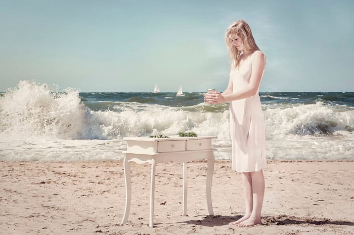 Woman in white dress on beach with waves and sailboats