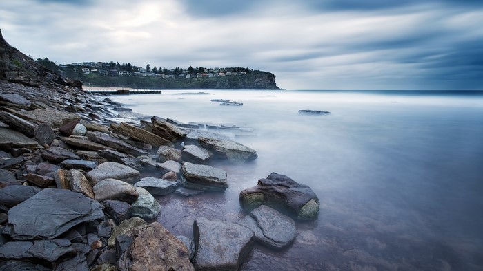 Rocky shore with calm ocean and distant town on cliff