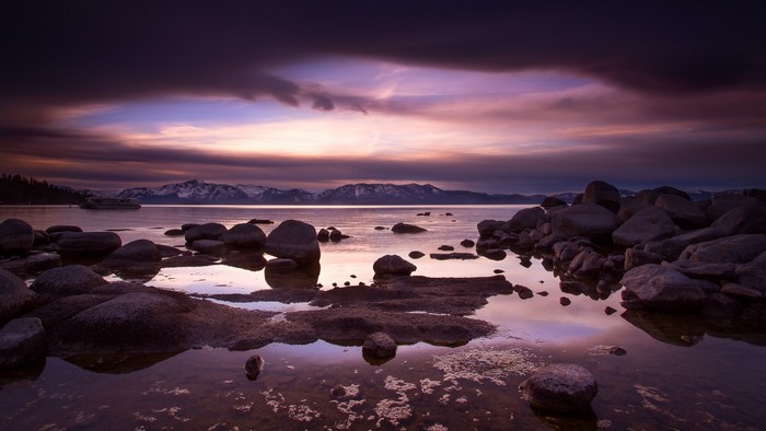 Sunset over a rocky lake shore with mountains