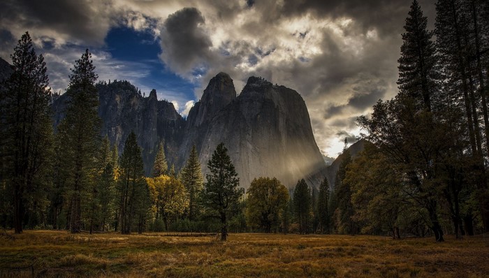 Sunlight beams through clouds onto Yosemite National Park mountains and trees
