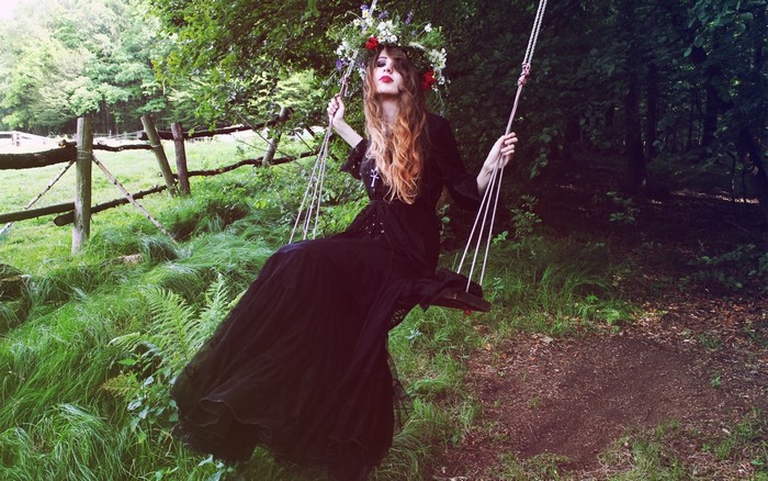 Woman in black dress on a swing in a forest