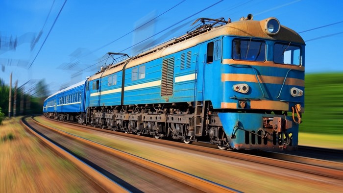 Blue and yellow electric locomotive pulling passenger cars on tracks