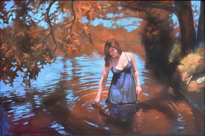 Woman in blue dress wading in water with autumn leaves