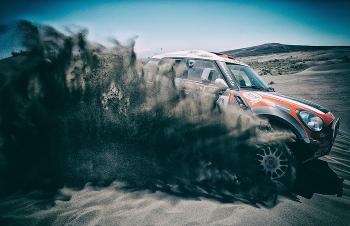 Mini Cooper rally car kicking up sand in a desert