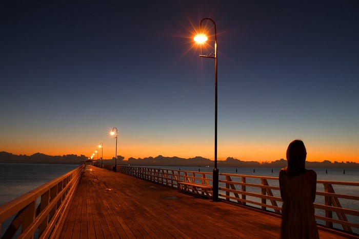 Woman on a pier at sunset with streetlights