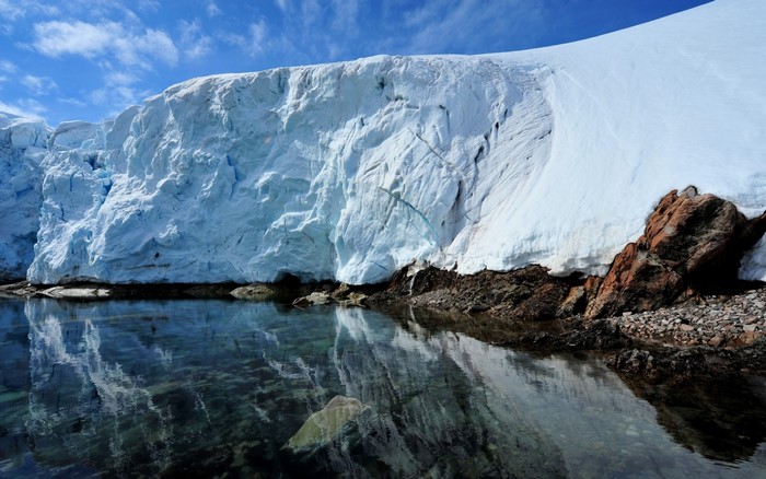 Glacier wall reflecting in clear water with rocky shore