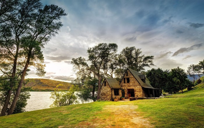 Stone cottage by a lake with trees and hills