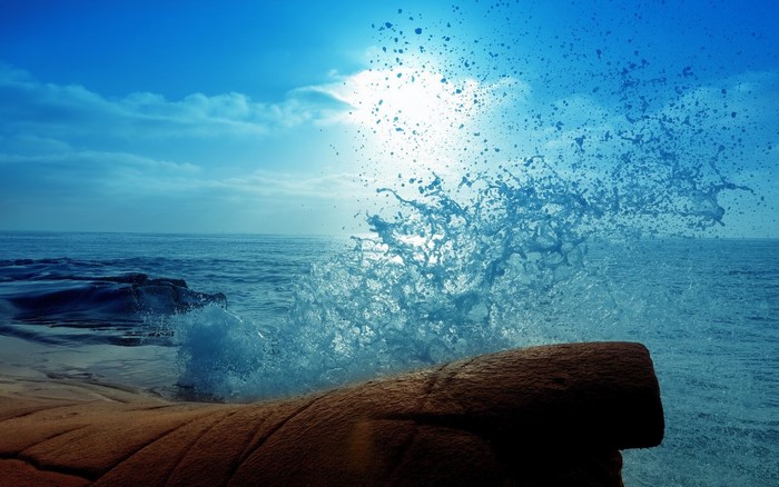 Ocean wave splashing on rocks under sunlight