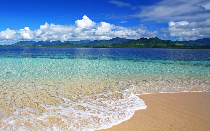 Crystal clear water on a sandy beach with mountains in the background