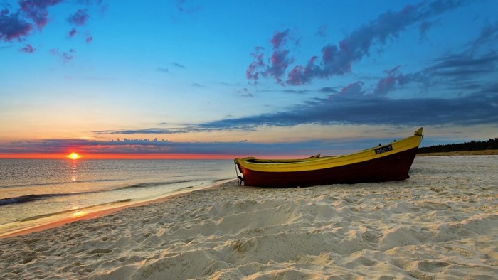 Boat on a sandy beach at sunset over the sea