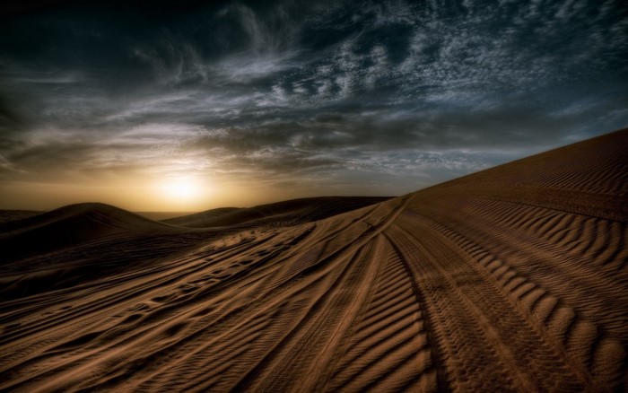Desert sand dunes at sunset with tire tracks