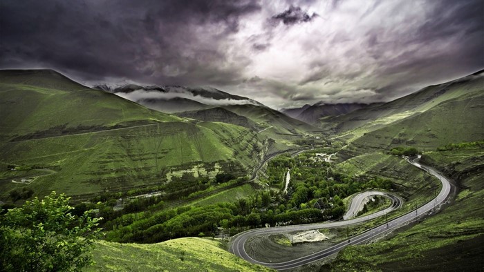 Winding road through a green mountain valley under a cloudy sky