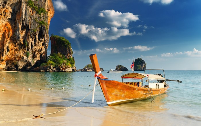 Long tail boat on a tropical beach with limestone cliffs