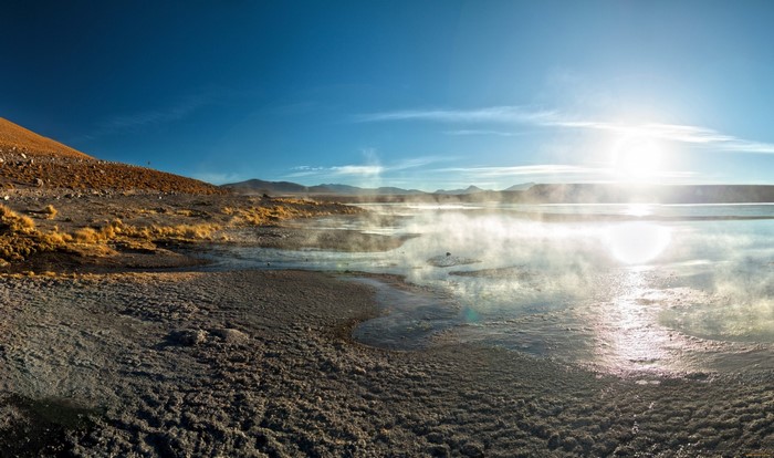 Geothermal landscape with steam rising from a body of water under a bright sun