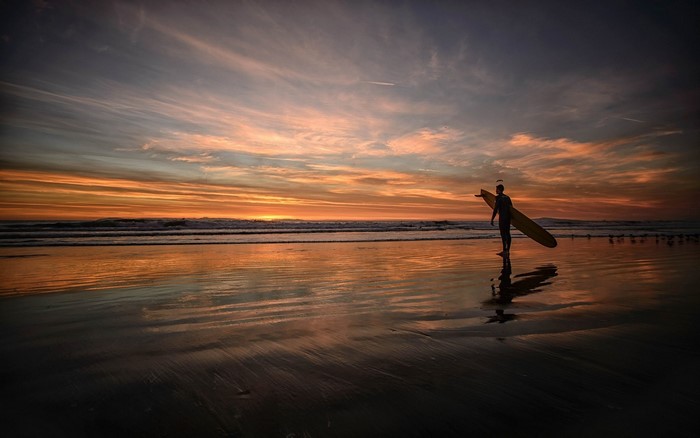 Surfer with surfboard on beach at sunset