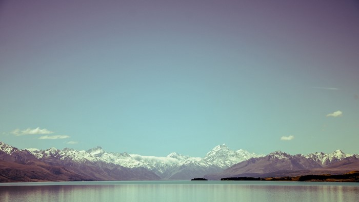 Snow-capped mountains reflected in a calm lake under a gradient sky